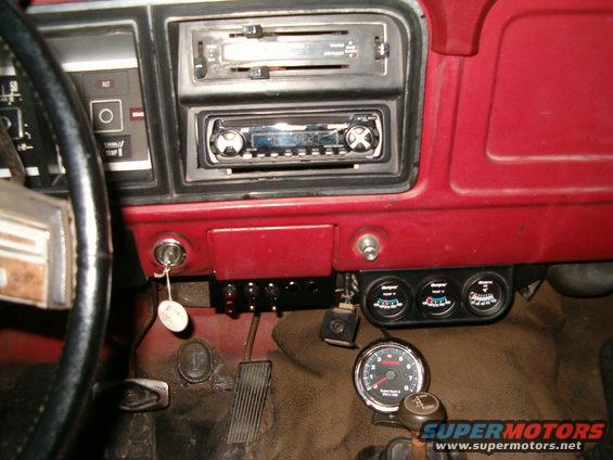 Dashboard interior with steering wheel, radio, and aftermarket gauges. Shows a tachometer and three other gauges below the dash