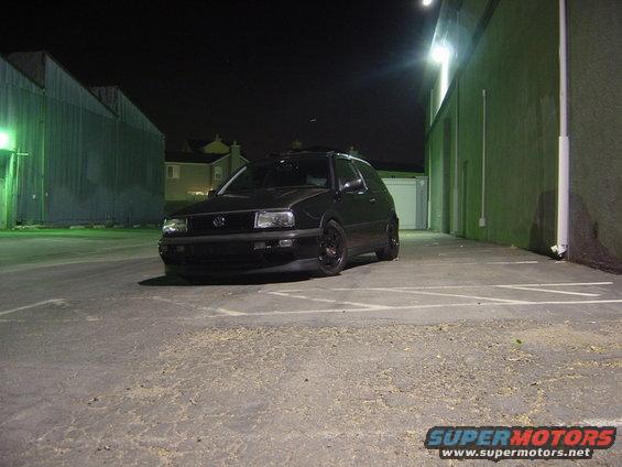 Black Volkswagen Golf Mk3 parked in a lot at night. The grille and headlight design are visible
