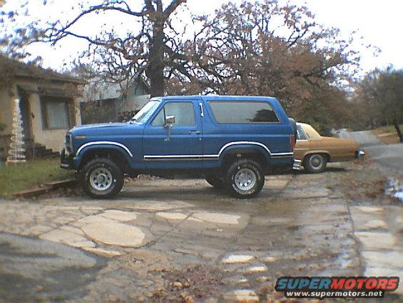 Blue SUV with chrome trim parked on cracked concrete, side view. Another car is parked behind it