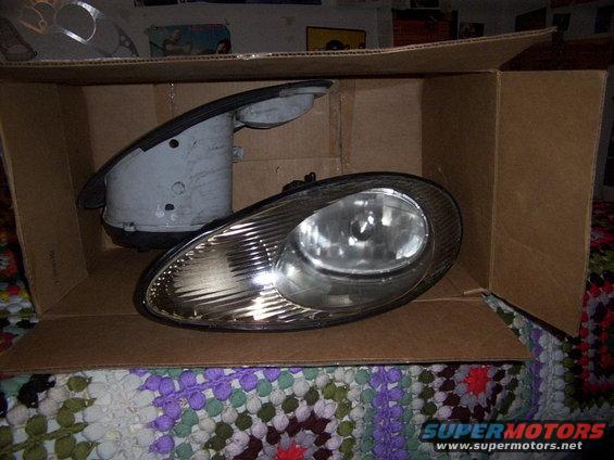 two car headlights, one with housing, sitting in a cardboard box