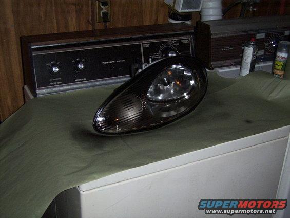Black headlight with clear lens and internal reflectors sits on a green cloth over a white appliance