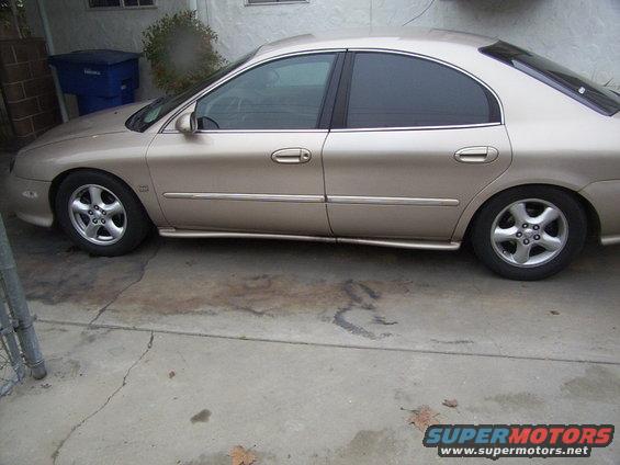 Tan sedan parked in a driveway. Side view shows tinted windows and alloy wheels