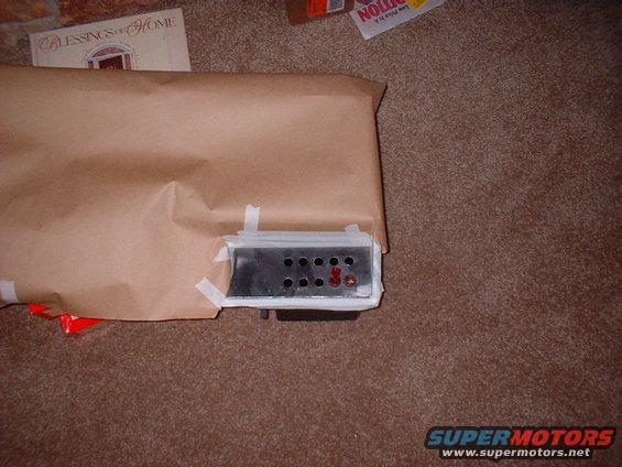 Car part, possibly a radio or control unit, wrapped in brown paper with tape