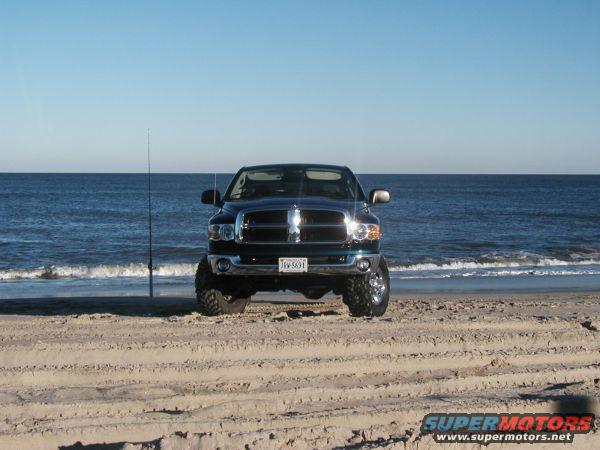 2004 Dodge 2500 parked on a sandy beach with the ocean in the background. License plate JVV 5691 is visible