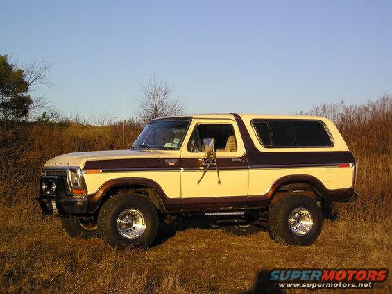 Two-tone beige and brown 1978 Ford Bronco with chrome wheels parked in dry grass