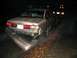 1999 Ford Crown Victoria - A damaged 1990s Ford Crown Victoria is seen from the rear, its bumper hanging off, on a dark, wet road.