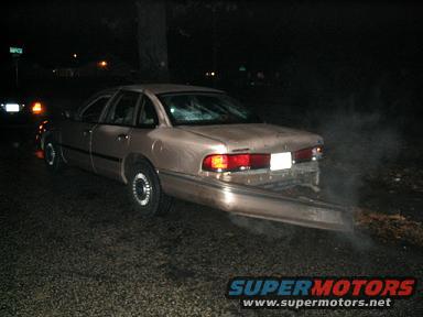 Tan sedan with rear bumper detached, smoke coming from underneath