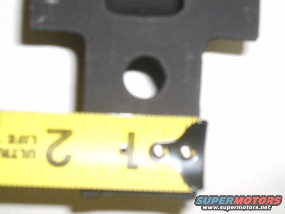 Black metal shackle mount with a hole, measured by a yellow tape measure showing 2 inches