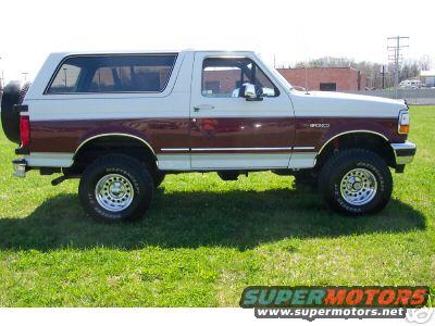 Two-tone white and maroon Ford Bronco parked on grass. Spare tire mounted on rear door