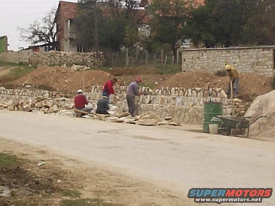 Masons building a new wall. The ones sitting are hand shaping the pieces of rock with hammers for the perfect fit.