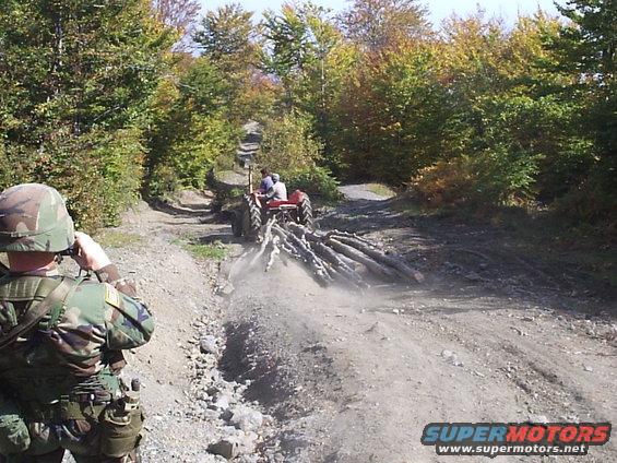 Tractor pulling logs up a dirt road, soldier watches