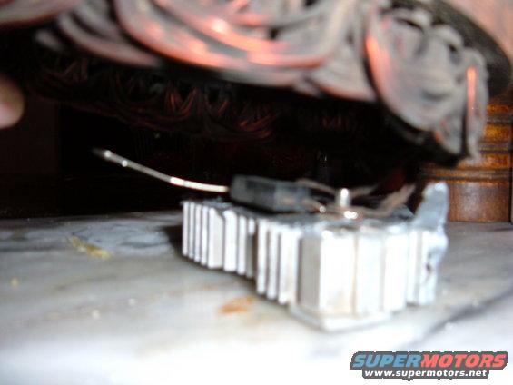 Close-up of an alternator voltage regulator with wiring. The Supermotors.net logo is visible