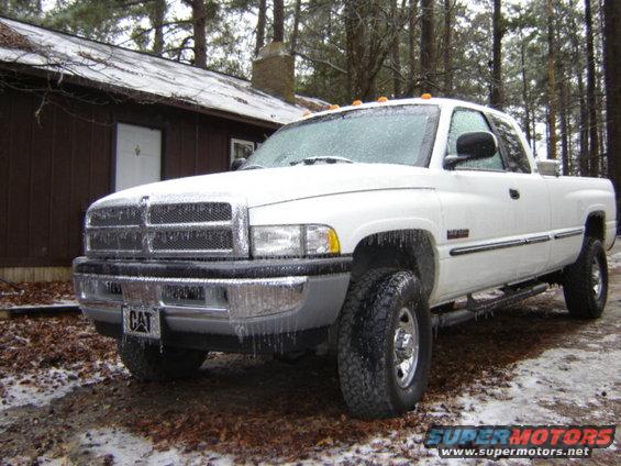 White Dodge Ram pickup truck covered in ice, parked in front of a cabin
