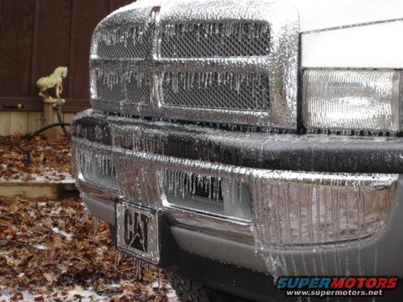 Truck grille and bumper covered in ice, with icicles hanging down. A CAT license plate is visible