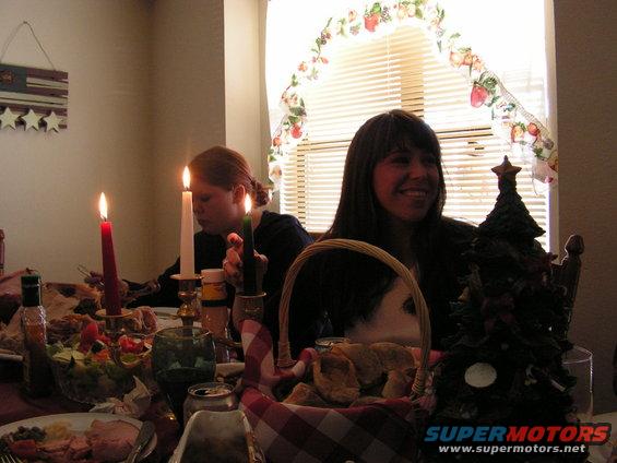 Two women sit at a dinner table with candles and food, a Christmas tree decoration is visible