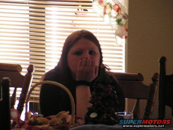 Woman with hand over mouth sitting at a table with blinds and a small Christmas tree