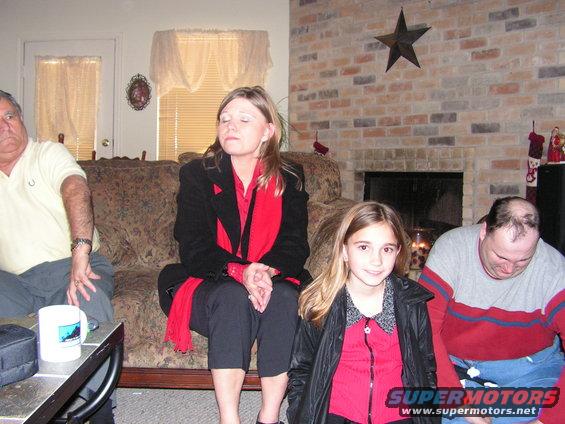 Four people sit on a couch and floor in front of a brick fireplace