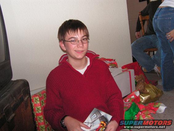 Boy in red sweater holding a booklet, surrounded by Christmas gifts
