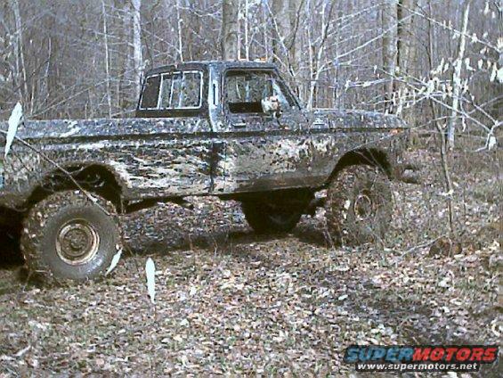 Mud-covered 1978 Ford F-250 pickup truck driving off-road in a wooded area