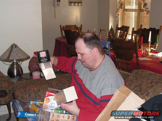 Man opening a gift box with Phillips 66 logo. Other gifts and board games are visible