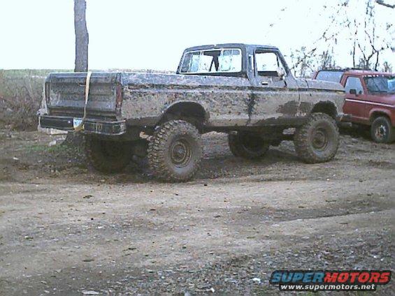 Muddy pickup truck with large tires, parked next to a red pickup truck