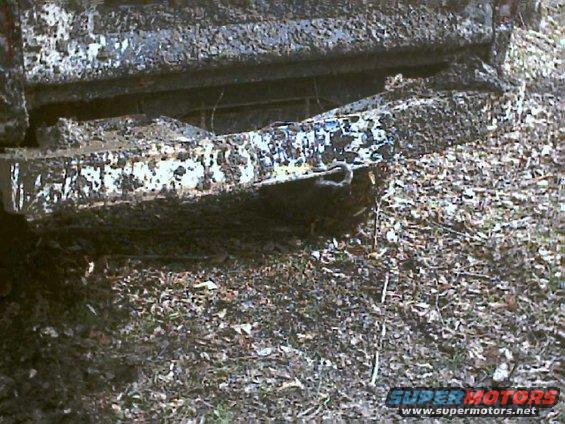 Mud-covered truck bumper with a tow hook, seen from the rear