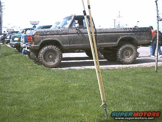 Mud-splattered dark green 1973 Ford F-Series pickup truck, lifted with large tires, parked on grass