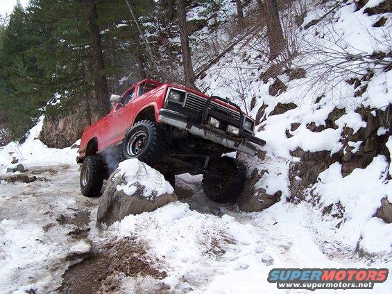Red truck with large tires navigating a snowy, rocky trail