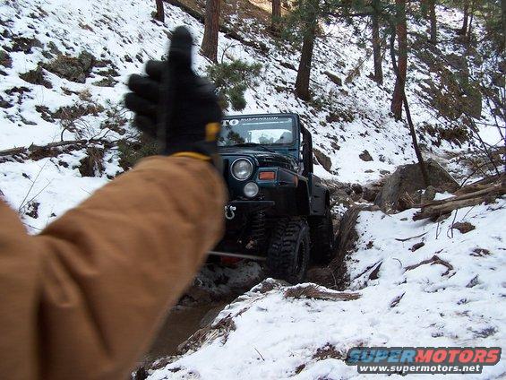 Jeep Wrangler navigating a snowy, rocky trail with a person giving a thumbs up