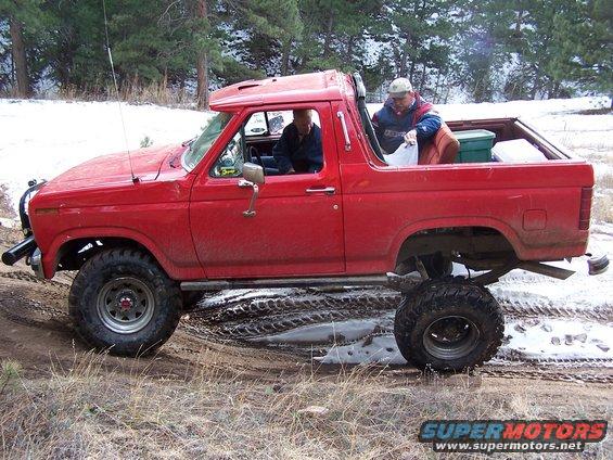 Red lifted 1980s Ford Bronco driving through mud and snow