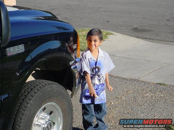 Black 1999 Ford F-250 front fender and tire with a boy standing nearby