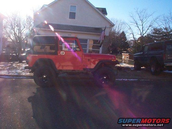 Red Jeep YJ with black hardtop, lifted suspension, and large tires, parked on a street