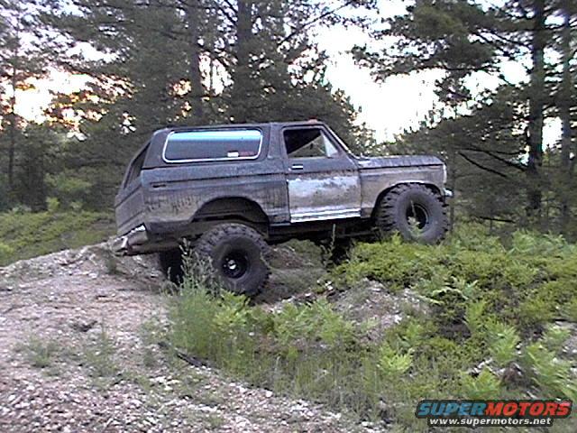 Dark gray Ford Bronco with a white cap driving off-road on a dirt hill
