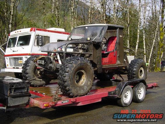 Custom off-road vehicle with red seats on trailer, RV in background