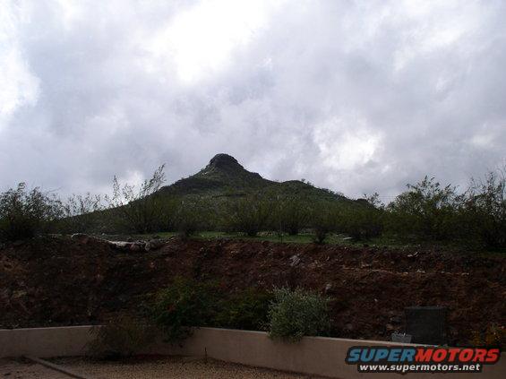 Mountain peak under cloudy sky, with scrub brush and dirt in foreground