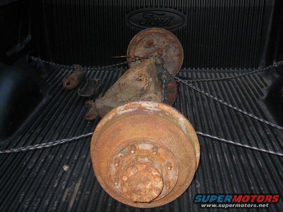 Rusty rear axle assembly with dual wheels, secured with chains in a truck bed