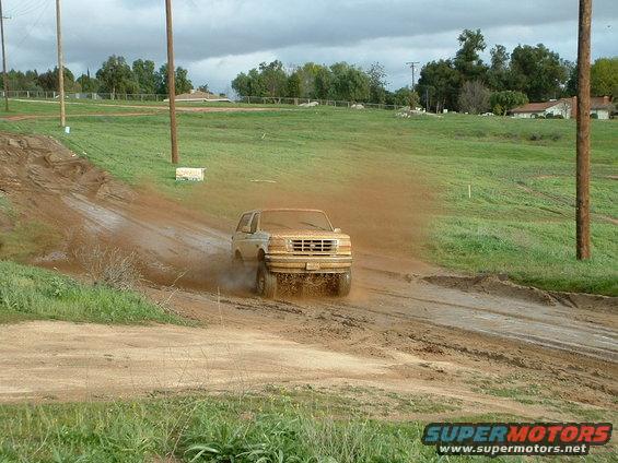 Tan 1995 Ford Bronco driving through mud, front view