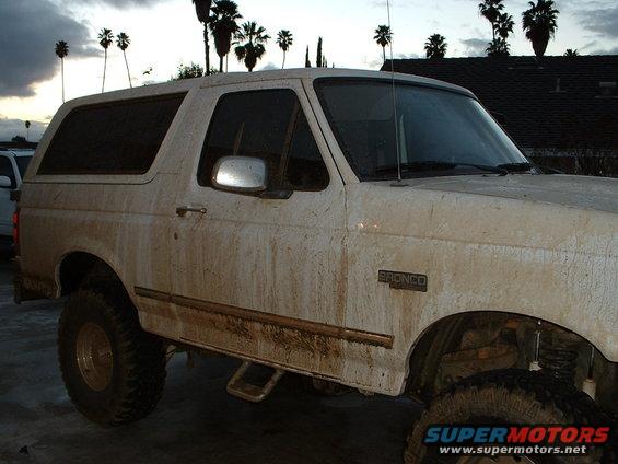 White 1995 Ford Bronco, covered in mud, viewed from the front-right