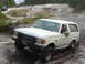 1993 Ford Bronco - A white Ford Bronco navigates a muddy off-road course with another vehicle in the background.