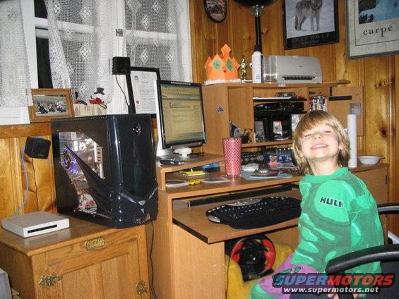 Kid in Hulk shirt at computer desk with gaming wheel and large PC tower