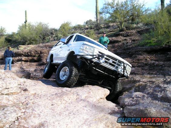 White Ford Bronco with aftermarket bumper and lift kit navigating rocky terrain