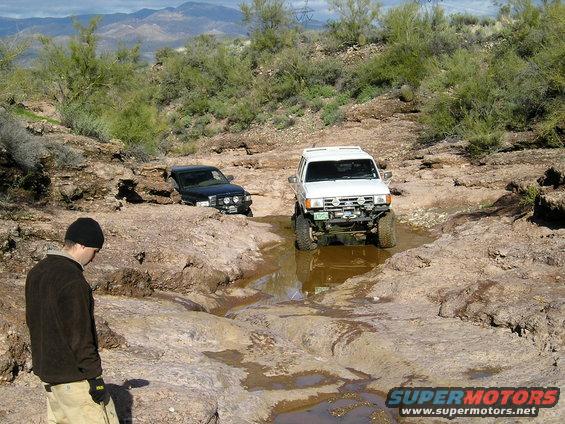 White SUV off-roading, front view. Black SUV stuck in background