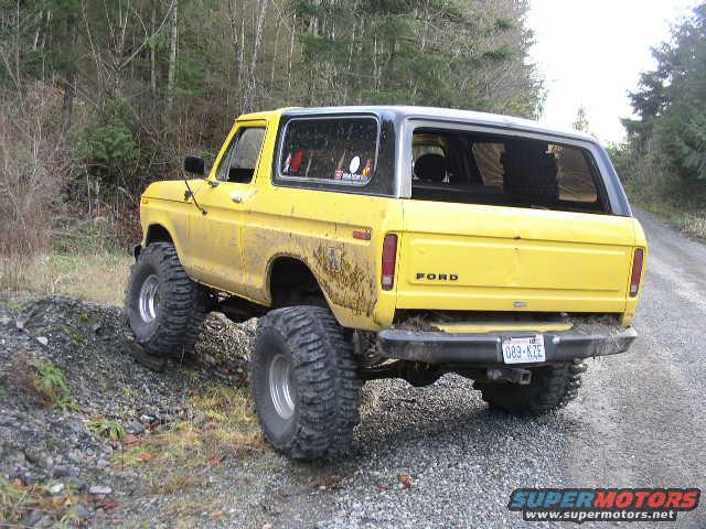 Yellow 1978 Ford Bronco with large off-road tires parked on a gravel road next to a rocky incline