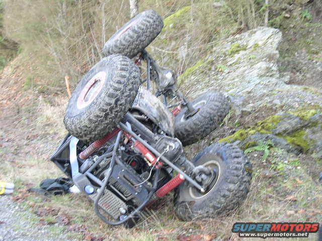 Off-road vehicle overturned on grassy slope, showing exposed roll cage and large tires