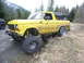 1978 Ford Bronco - This lifted Bronco is parked on a grassy incline next to a dirt road, with a wooded mountainside behind it.