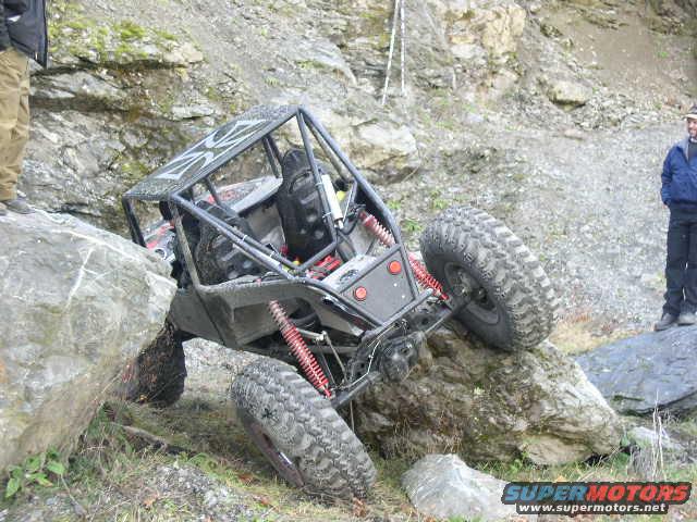 Off-road buggy with a roll cage and large tires navigating rocky terrain