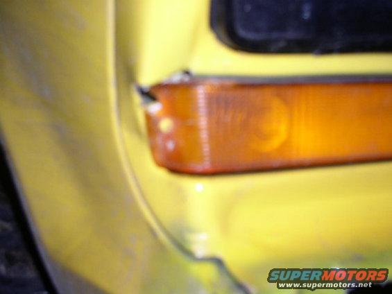 Close-up of a yellow vehicle's fender and amber marker light. Supermotors.net logo visible