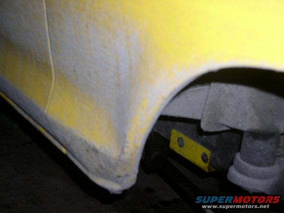 close-up of yellow vehicle fender with primer and suspension parts visible