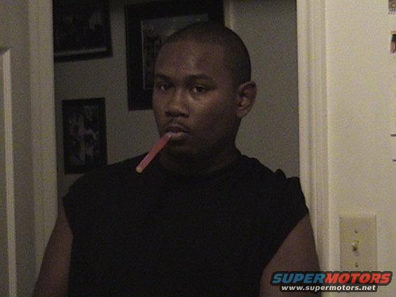Man in black shirt with a pink object in his mouth, indoors