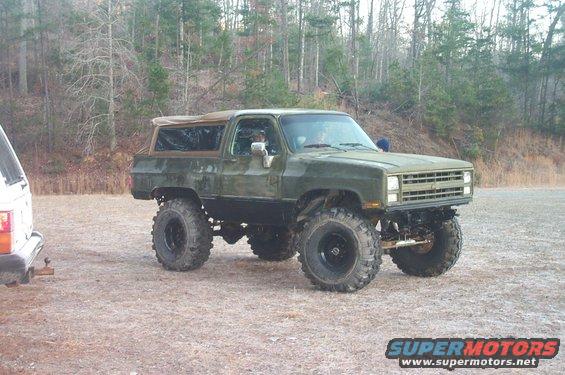 Lifted green SUV with large tires parked next to a white SUV